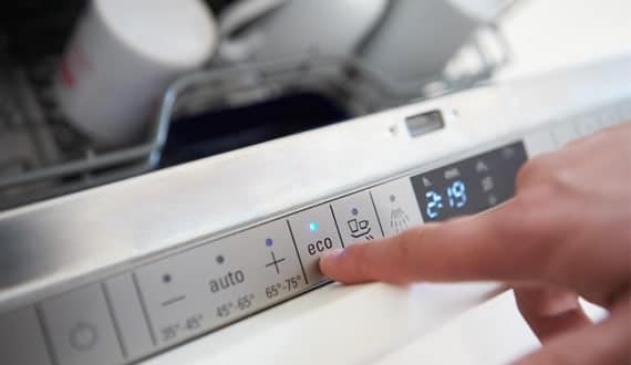 finger pushing the eco button on a modern dishwasher